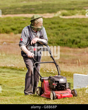 Uomo che indossa un capo net durante il taglio dell'erba in chiesa Strandakirkja, penisola di Reykjanes, Islanda Foto Stock