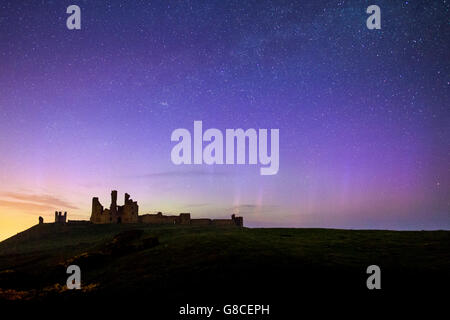 La Northern Lights delicatamente la danza dietro le rovine del castello di Dunstanburgh, Northumberland, Regno Unito Foto Stock