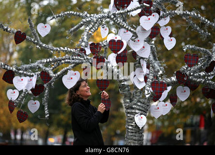 Sally McNaught di Poppy Scotland allega messaggi di sostegno alla scultura ad albero che è stata piantata accanto al campo della memoria di Edimburgo, al quale saranno allegati più di un migliaio di messaggi di sostegno scritti su carte a forma di cuore, prima dell'apertura di lunedì. Poppyscotland invita il pubblico a piantare croci sul campo durante la settimana del papavero (da lunedì), in cambio di una donazione, con l'ambizione di riempire il campo da Armistice Day. Foto Stock