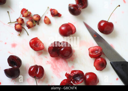 Fresche ciliege rosse, alcuni interi, altri snocciolate con pila di box e coltello seghettato Foto Stock