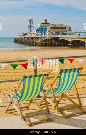 Sedie a sdraio e lavorati a maglia bunting al mare con spiaggia di Bournemouth e pier in giugno Foto Stock