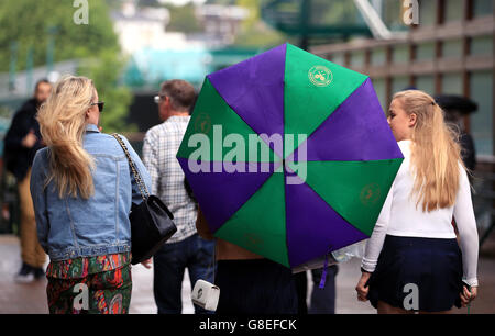 Spettatori riparo dalla pioggia sotto un marchio di Wimbledon ombrello della seconda giornata dei campionati di Wimbledon al All England Lawn Tennis e Croquet Club, Wimbledon. Foto Stock