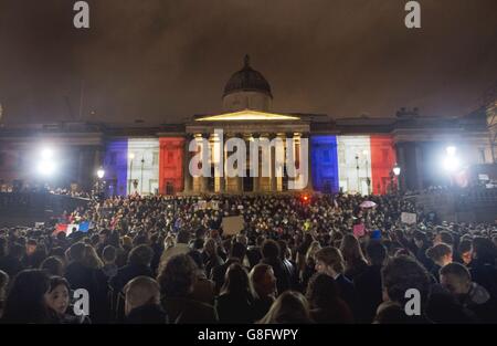 La Galleria Nazionale è illuminata nei colori del Tricolore Francese mentre la gente si riunisce durante una veglia a Trafalgar Square, a Londra, poiché Londra si trova in solidarietà con la sua sorella capitale europea sulla scia di una serie di attentati terroristici coordinati a Parigi il venerdì sera, che ha causato almeno 127 morti e oltre 200 feriti. Foto Stock