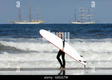 I surfisti sulla spiaggia di Tynemouth sfidano il Mare del Nord mentre le navi Tall passano sulla loro strada per il fiume Tyne. Più di 100 navi tradizionali si sono radunate sul fiume come parte di uno dei più grandi eventi all'aperto che si sono tenuti nel paese quest'anno. La Newcastle Gateshead Tall Ships' Race inizia oggi dopo tre anni di pianificazione ed è probabile che attragga più di un milione di visitatori a Tyneside. Foto Stock