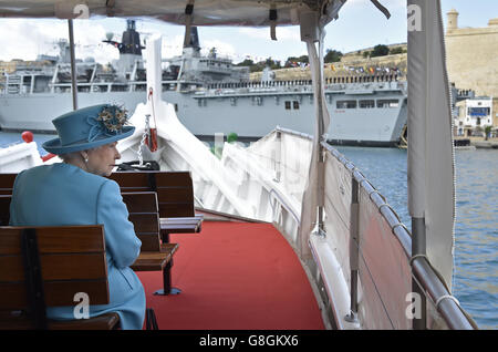 La regina Elisabetta II visita il Grand Harbour a bordo di una tradizionale barca da pesca maltese, con la nave d'assalto anfibia HMS Bulwark vista sullo sfondo. Foto Stock