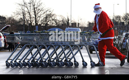 Un uomo vestito da padre Christmas raccoglie i carrelli in un supermercato Morrisons a Belle vale, Liverpool. Foto Stock