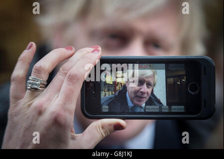 Il sindaco di Londra Boris Johnson è intervistato dalla BBC su un telefono cellulare dopo aver provato la mano a tagliare le chiavi e le scarpe da menzare a Timpson, nella città di Londra, dove ha incontrato ex-trasgressore, Russell Zecanovsky, che è stato impiegato da Timpson come parte della loro politica di reclutamento ex-trasgressori. Foto Stock