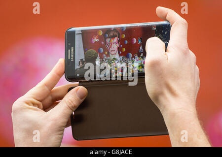 Un uomo scatta una foto su uno smartphone di un murale del musicista David Bowie, a Brixton, a sud di Londra, dopo l'annuncio di questa morte ieri. Foto Stock