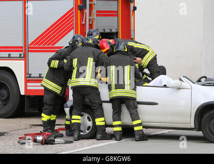 Coraggiosi vigili del fuoco alleviare un infortunato dopo incidente di automobile Foto Stock