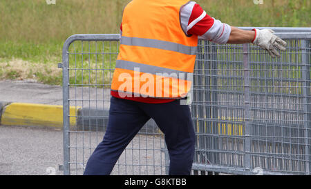 Lavoratore con alta visibilità giacca riflettente si muove il ferro ostacoli prima dell'evento sportivo Foto Stock