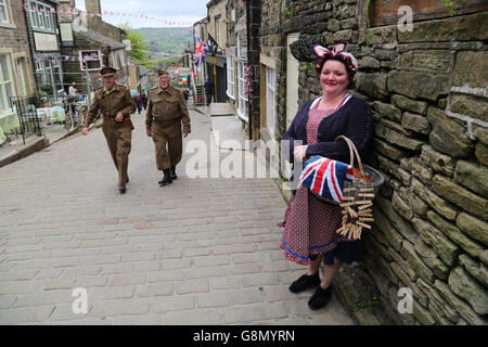 Una donna in costume sorrisi come due uomini vestiti in casa della guardia uniformi a piedi passato durante l annuale 1940 evento in Haworth. Foto Stock