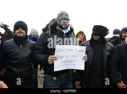 I migranti protestano mentre continuano le demolizioni nel campo migrante di Calais, noto come la giungla, nella Francia settentrionale. Foto Stock