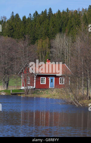 Rossa svedese cabina in legno lungo il fiume in primavera, Värmland, Svezia Foto Stock