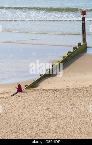 Giovane donna che indossa un cappello e utilizzando il telefono cellulare mentre è seduto sul groyne a Bournemouth Beach nel giugno Foto Stock