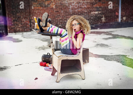 Carino dai capelli ricci ragazza seduta in un banco di scuola in ambiente urbano Foto Stock