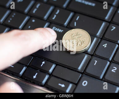 British una sterlina moneta giacente sulla tastiera del laptop con il dito premendo il tasto Invio Foto Stock