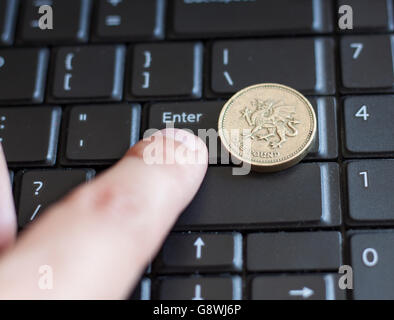 British una sterlina moneta giacente sulla tastiera del laptop con il dito premendo il tasto Invio Foto Stock