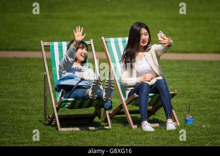 Due donne si godono il sole sulle sedie a sdraio a St James Park, Londra, in quanto molte parti del Regno Unito godono una giornata di clima caldo. Foto Stock