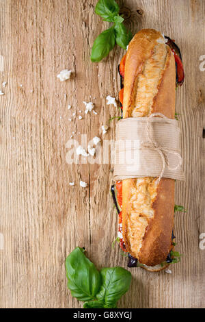 Tappezzate vegetariano sottomarino baguette sandwich con melanzane alla griglia, pepe e formaggio feta sul tagliere di legno oltre il buio Foto Stock