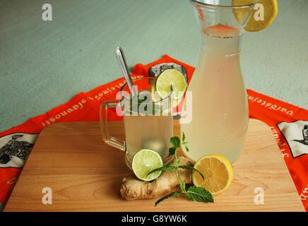 Lo zenzero e il succo di limone in un bicchiere e brocca plank zenzero, limone, lime e foglie di menta su uno sfondo colorato Foto Stock