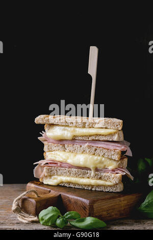 Grano intero grigliato pane sandwich con fusione a caldo, formaggio prosciutto e basilico sul tagliere di legno su sfondo scuro. Foto Stock