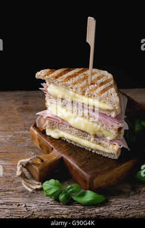 Grano intero grigliato pane sandwich con fusione a caldo, formaggio prosciutto e basilico sul tagliere di legno su sfondo scuro. Foto Stock