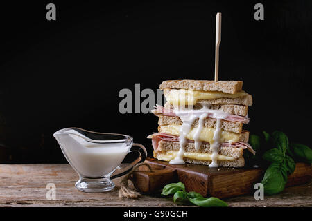 Grano intero grigliato pane sandwich con fusione a caldo, formaggio prosciutto, basilico e versare la salsa bianca sul tagliere di legno su dar Foto Stock