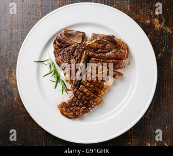 Tagliate a fette grigliate di T-Bone Steak sulla piastra bianca su sfondo di legno Foto Stock