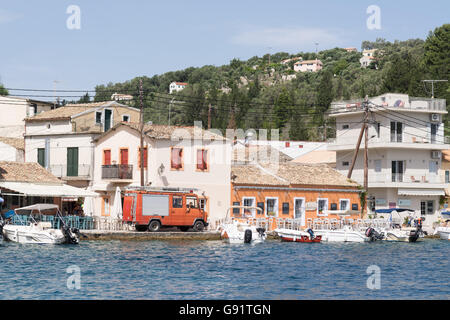 Paxos, Grecia - motore Fire negoziando con cautela la stretta strada tra i tavoli e le sedie e il mare nel villaggio di Loggos Foto Stock