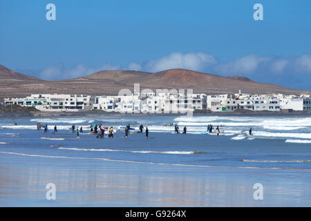 Surfisti sulla spiaggia Playa de Famara guardando verso Caleta de Famara village, Lanzarote Foto Stock