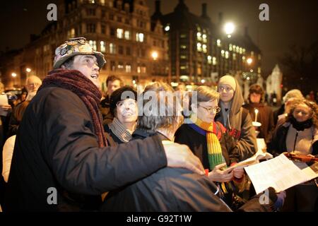 Il protestore anti-guerra Brian Haw è affiancato da circa 100 cantanti di carol in Piazza del Parlamento. Questo concerto di Carol sta infrangendo la legge essendo all'interno della zona di esclusione della Camera dei Comuni. Il concerto è andato senza incedenti. Foto Stock