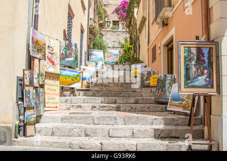 Scena di strada a Taormina, Italia. Dipinti in vendita visualizzati entrambi i lati della scalinata in ciottoli che conducono fuori corso Umberto Foto Stock