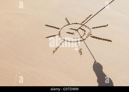 Ombra mano che tiene un bastone con il disegno di una faccina sorridente sole su una spiaggia. Regno Unito Foto Stock