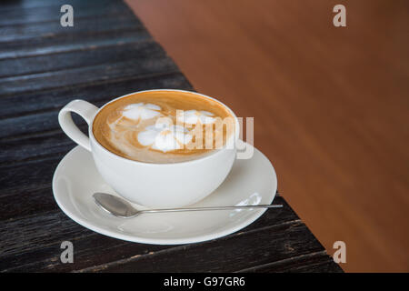 Una tazza di caffè con pattern di fiori in una tazza bianca su sfondo di legno. Foto Stock