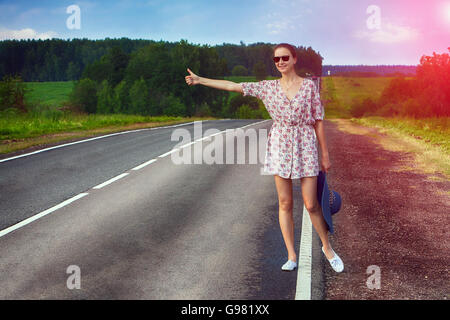 Attraente giovane donna autostop lungo una strada. Foto Stock