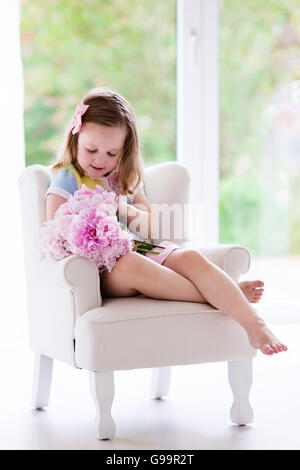 Bambina maleodoranti peonia mazzo di fiori seduto in una sedia bianca nella soleggiata camera da letto. Vivaio interno con i fiori per le ragazze Foto Stock