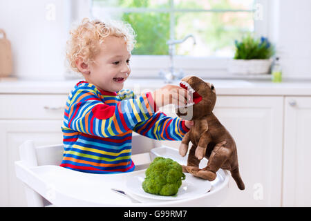 Happy Baby sitting in alta sedia di mangiare i broccoli in una cucina bianca. Una sana alimentazione per i bambini. Bio verdura come cibo solido Foto Stock