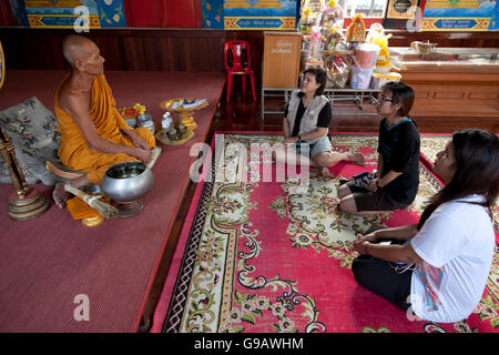 Un monaco della chat con tre donna tailandese dopo che hanno fatto offerte e preghiere condotte nel tempio principale hall di Wat Phummarin in M Foto Stock