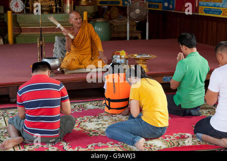 Un monaco utilizzando un fascio di canne di spruzzare acqua santa su un gruppo di Thais pregando nel tempio principale hall di Wat Phummarin in Ma Foto Stock