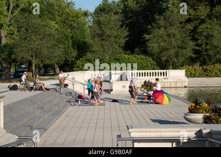 Classe di yoga all'aperto in un parco, accompagnato dal musicista a suonare la chitarra. Foto Stock