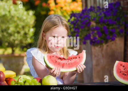 Felice ragazza con big red fetta di anguria seduto su rustiche tabels in giardino estivo. Foto Stock