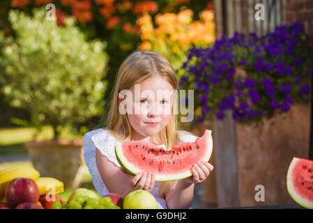 Felice ragazza con big red fetta di anguria seduto su rustiche tabels in giardino estivo. Foto Stock