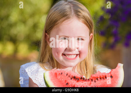 Felice ragazza con big red fetta di anguria seduto su rustiche tabels in giardino estivo. Foto Stock