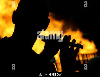 Un uomo gioca un flauto di fronte a un falò sulla strada Shankill a Belfast, Irlanda del Nord, dove centinaia di incendi sono stati fissati alla mezzanotte per commemorare la vittoria del principe protestante William sul re cattolico Giacomo II nella battaglia di Boyne nel 1690. Foto Stock