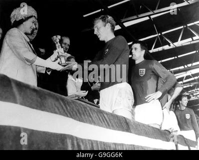 Il capitano inglese Bobby Moore viene presentato con la Coppa del mondo trofeo di sua Maestà la Regina come Geoff Hurst guarda su in awe Foto Stock