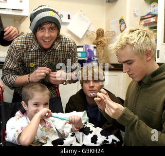 Regan Gibbs, 5 anni, dalle Isole Shetland (centro), disegna una faccia sorridente sulla fronte di Tom Fletcher (a destra), mentre visita il Great Ormond Street Children's Hospital con i suoi compagni di banda a McFly (da sinistra a destra) Danny Jones e Dougie Poynter. Foto Stock