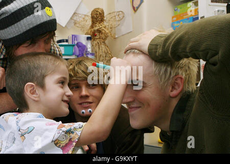 Regan Gibbs, 5 anni, dalle Isole Shetland (centro), disegna una faccia sorridente sulla fronte di Tom Fletcher (a destra), mentre visita il Great Ormond Street Children's Hospital con i suoi compagni di banda a McFly (da sinistra a destra) Danny Jones e Dougie Poynter. Foto Stock