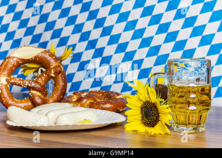 Bicchiere pieno di birra con prezels e tradizionale salsiccia bavarese nella parte anteriore della bandiera bavarese Foto Stock