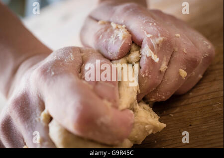 Close-up di due forti mani di un fornaio che sono manualmente gli impasti su una ruvida, cucina in legno tabella Foto Stock