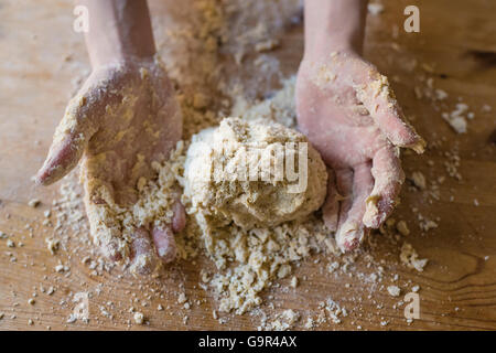 Close-up di due forti mani di un fornaio che sono manualmente gli impasti su una ruvida, cucina in legno tabella Foto Stock